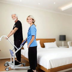 Two people in a bedroom setting with one pushing a mobility aid.