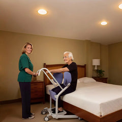 Woman assisting an elderly person using a patient transfer device lift in a bedroom setting.
