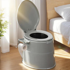 Portable toilet on a wooden floor next to a bed with white bedding.